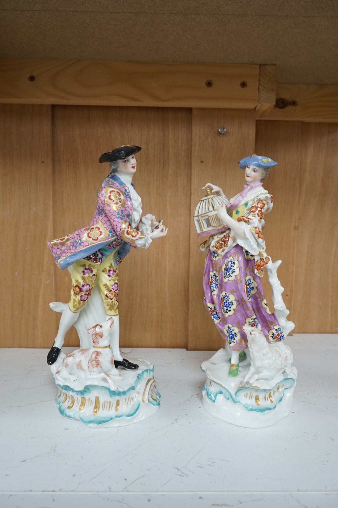A pair of Derby style figures of a lady holding a bird cage and a gentleman holding a bird, tallest 23cm high